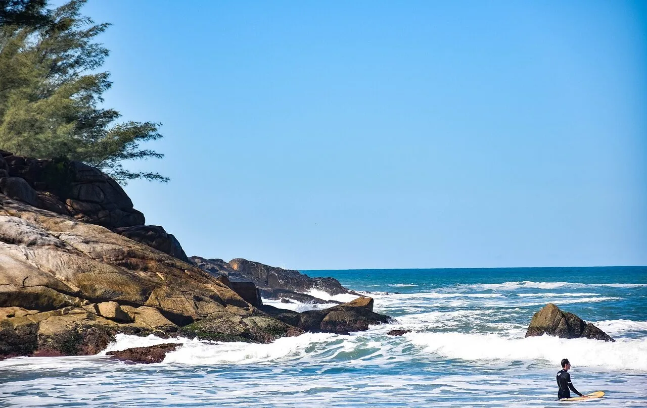 Praia de Florianópolis com ondas, pedras e um surfista