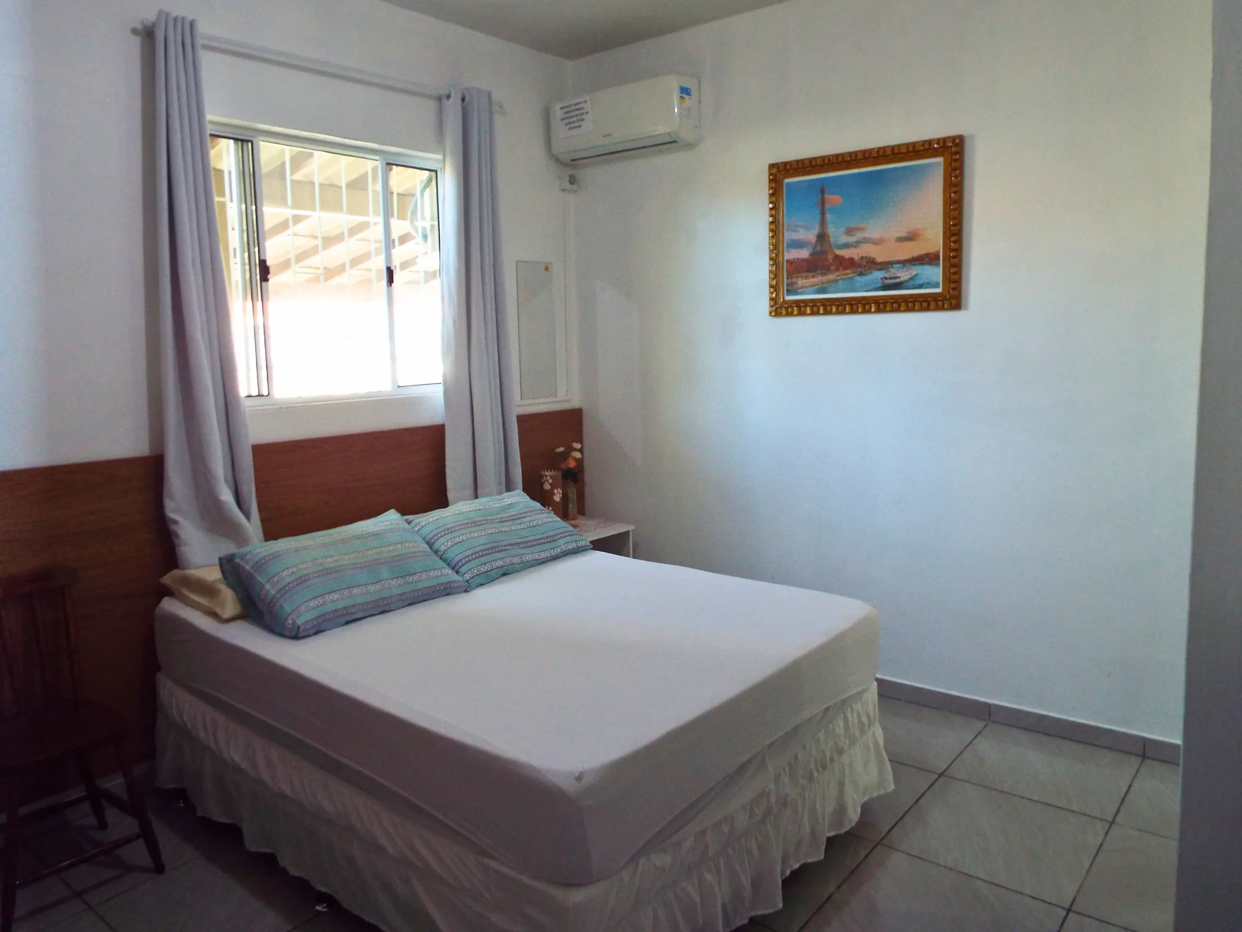 Suite numero 10, com cama de casal uma cadeira, quebra-cabeça pendurado, ar condicionado e janela ampla