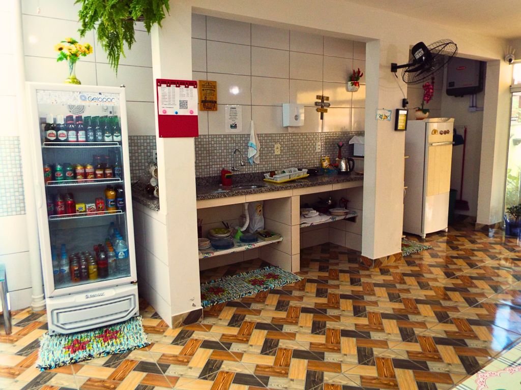 Cozinha equipada da Pousada SolRiso, contendo expositor, geladeira, pia de pedra, forno elétrico, microondas e outros eletrônicos
